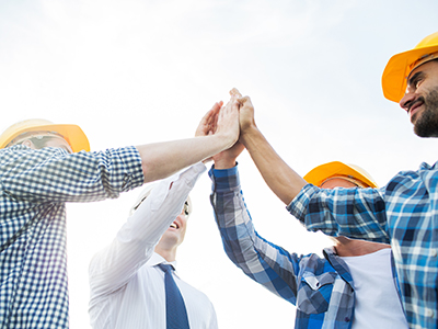 Workers in hard hats giving each other a group high five while they are outdoors